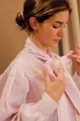 Camisa de algodón a rayas verticales rosas y blancas, con cuello alto y lazo grande en el cuello.