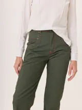 Jean recto de gabardina gastada color verde militar, con pespuntes y atraques en hilo rojo. Presenta bolsillos delanteros con forma curva y cierre frontal.