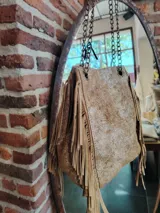 Bolso bandolera de cuero color dorado con textura craquelada y flecos largos en los laterales. Tiene cadena metálica dorada y herrajes dorados.