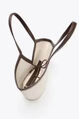 Bolso tipo shopper color crudo, con cuerpo de lona y detalles en cuero marrón. Tiene doble asa de hombro y una bolsa interior extraíble con cierre de cremallera. Se cierra con un lazo.