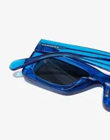 Lentes de sol unisex Hawkers Paula Echevarría, modelo Lauper, con montura rectangular de acetato color azul eléctrico y lentes grises.