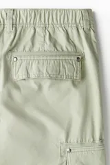 Pantalón cargo color verde claro, de corte relajado, con bolsillos laterales con solapa y botón a presión. Confeccionado en popelina de algodón con elástico en la parte posterior de la pretina y cierre con botón a presión.