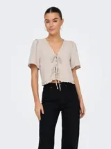 Blusa color gris claro con escote en V, mangas cortas abullonadas y detalle de encaje en el escote y ruedo. Se cierra con lazos en el frente.