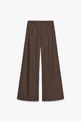 Pantalón blanco de lino, de corte ancho y tiro medio, con cintura elástica ajustable con cordones y bolsillos laterales.