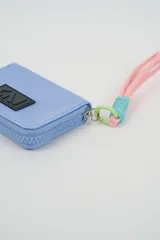 Billetera compacta de color fucsia con cierre perimetral y parche frontal con logo CNI en negro. Incluye una correa de muñeca de cordón en tonos rosado y celeste con un gancho de sujeción verde.