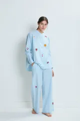 Conjunto de pijama celeste a rayas verticales blancas, compuesto por una camisa de manga larga con cuello mao y botones, y un pantalón de corte recto. La camisa y el pantalón tienen bordados de corazones, soles y otros motivos.
