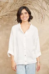 Camisa blanca de lino con cuello mao, mangas 3/4 con botón para sujetar, cierre con botones a tono y ajuste con cordón en la cintura.