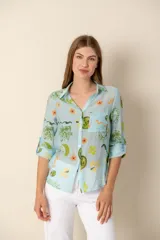 Camisa celeste con estampado de soles, lunas, flores y tortugas en tonos verdes, amarillos y naranjas.