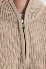 Sweater de punto inglés color beige, de manga larga y cuello alto con cierre metálico frontal.