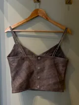 Top de cuero color marrón con escote en V y tirantes finos trenzados. Cuenta con un detalle vertical de pasamanería artesanal bordada a mano en el frente y cierre con broches en la espalda.