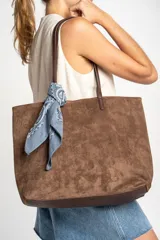 Bolso tipo tote de gamuza vegana color camel, con asas de mano y logo grabado en el frente.