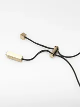 Collar con cordón negro largo y regulable, con un dije triangular de acabado brillante, posiblemente esmaltado o lacado, con un borde dorado y un orificio circular central. El cierre del cordón es ajustable mediante una pieza metálica dorada con terminales logotipados.