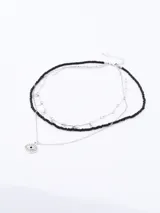 Collar plateado de tres capas: una de cuentas negras, una de cadena plateada con dijes circulares y una de cadena plateada con dije de ojo turco.