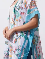 Kimono tejido con estampado floral multicolor, terminación de ruedo con borlas y mangas cortas con borde celeste.