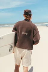 Buzo de tejido marrón con cuello polo y cierre parcial. Presenta un patrón texturado de espiga y el estampado frontal en blanco con el texto "glassywave".