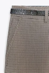 Pantalón de tiro alto con estampado a cuadros en tonos beige y marrón, con bolsillos delanteros y falsos bolsillos traseros. Incluye cinturón marrón con hebilla metálica.