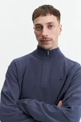 Sweater verde oliva de punto con cuello alto y cierre de medio cierre. Tiene puños y logo bordado en el pecho.