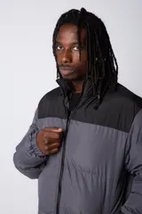 Campera puffer gris con la parte superior negra, cierre frontal y cuello alto.