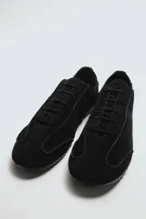 Zapatilla de cordones color negro, con capellada de cuero serraje, horma redonda y suela ultrafina.