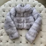 Chaqueta corta de piel sintética color gris con cuello alto y cierre metálico.