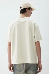 Remera color crema de punto pesado con cuello redondo ribeteado, hombros caídos y bajo recto. Corte holgado confeccionada con tejido funcional Coolmax, una fibra de poliéster de secado rápido que elimina la humedad y regula la temperatura corporal.