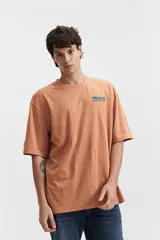 Remera de manga corta color salmón, de corte holgado con estampado en la espalda que incluye una flor con cara y texto.