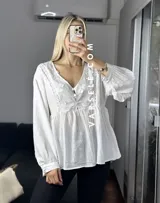 Blusa color crema con escote en V, mangas largas abullonadas con puños elásticos y detalles de encaje y bordado en el frente.
