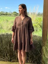 Vestido corto color marrón, de lino, con cuello mao, escote con botones de nácar, mangas 3/4 con volados y falda con volados en el ruedo.