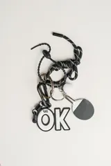 Llavero con dije de raqueta de ping pong, pelota blanca, dije con la palabra "OK" y cordón trenzado blanco y negro.