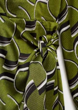Vestido corto de tejido fluido color verde con estampado abstracto en blanco y negro. Diseño cruzado con cuello camisero, mangas largas y cierre de lazo lateral.