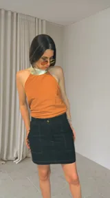 Minifalda negra de denim con pespuntes blancos contrastantes, tiro medio-alto y bolsillos frontales.