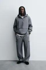 Pantalón cargo gris con textura acanalada, corte relaxed fit, cintura elástica con pliegues frontales, bolsillos laterales tipo cargo con solapa, bolsillos frontales y traseros de vivo, cierre frontal con cremallera y botón.