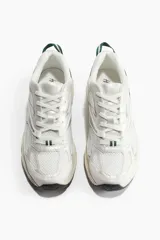 Championes deportivos blancos con detalles en verde y plateado, de malla y tejido revestido, con cierre de cordones y suela gruesa con diseño.