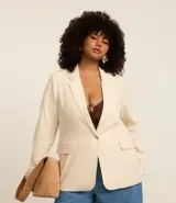 Blazer largo color crema confeccionado en viscosa y lino. Tiene solapas, mangas largas, bolsillos y cierre frontal con un botón.