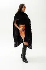 Ruana de tejido de punto color negro, confeccionada en lana merino. Presenta un diseño abierto con terminación de flecos en el ruedo.