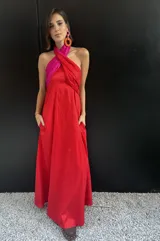 Vestido largo strapless con corpiño fruncido en color fucsia brillante y falda amplia en color rojo vibrante. La prenda tiene bolsillos laterales.