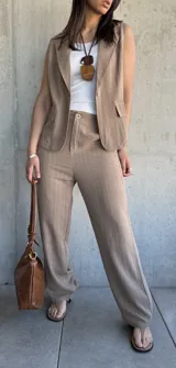 Conjunto sastrero tostado con rayas verticales finas, compuesto por un pantalón de corte recto y un chaleco sin mangas con solapas. El pantalón tiene cierre frontal con botón y bolsillos laterales. El chaleco tiene un botón frontal y bolsillos simulados.