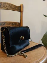Cartera bandolera negra de cuero con textura de pelo, cierre de broche metálico dorado y correa de cadena dorada.