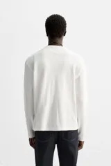 Camiseta blanca de manga larga con cuello redondo y textura cuadriculada.