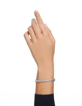 Brazalete rígido plateado con doble banda, una con piedras de talla baguette y otra con pavé de cristales blancos. Cierre a presión.