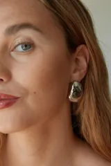 Aros tipo botón de acero quirúrgico hipoalergénico, con forma redondeada irregular y acabado brillante.