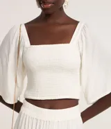 Blusa cropped color blanco, con escote recto, mangas amplias con elástico en los hombros, lastex en el cuerpo y textura.