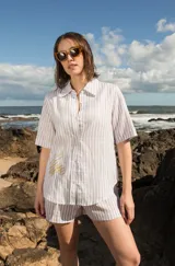 Camisa de lino a rayas verticales color naranja y blanco, de manga corta y corte oversize. Presenta bordados con motivos playeros en el frente y la espalda.