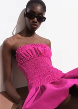 Vestido corto fucsia sin mangas, con escote recto, cuerpo fruncido y falda globo.