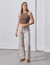 Pantalón de lino color beige con rayas verticales marrones, pretina ancha con punto smock y lazo ajustable, bolsillos verticales delanteros y bolsillos aplicados traseros.