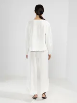 Camisa de lino color blanco, con cuello en V, manga larga con puños elásticos, cierre frontal con botones y dobladillo curvado.