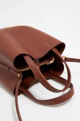 Bolso tote pequeño de cuero sintético color negro con doble asa de mano y correa bandolera ajustable y extraíble. Logotipo de la marca en letras doradas en la parte frontal.