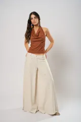 Pantalón súper campana de tiro medio color beige, confeccionado en lino con bordados, con bolsillos delanteros y traseros. Cierre frontal con cremallera y botón.