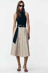 Vestido midi con falda beige con botones y cuerpo negro de cuello alto y sin mangas. Incluye cinturón negro con hebilla plateada.
