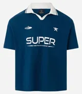 Remera de manga corta azul marino con cuello polo blanco. Presenta un estampado frontal en blanco con la palabra "SUPER" y un texto más pequeño debajo, junto con una estrella y un logo de platillo volante.